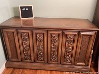 Front view of vintage wooden cabinet with ornate carved panels and woven side accents.