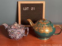 Both teapots side by side against a gray wall with LOT 21 sign.