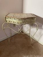 Full view of wicker and metal table showing wicker top and metal legs with floral design