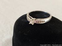 Front view of white gold diamond ring on black velvet display, showing central diamond and side stones.