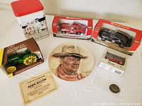 Overview of the lot showing John Wayne plate, John Deere model tractor box, two State Farm model car boxes, small collectible tin, small red fire truck, and coin