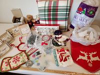 Photo showing assorted Christmas decor items including plaid pillow, plush bears, framed pictures, ribbons, oven mitt, synthetic blanket, and stocking with reindeer designs.