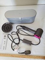 Supersonic hair dryer, power cord, diffuser attachment and storage case arranged on table.