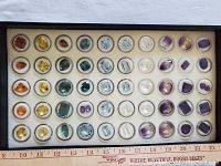Top-down view of black display box with 56 faceted gemstones in individual plastic vials on foam tray.