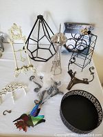 Full display of assorted metal decor items on white surface including stands, bowl, hook set, and ornaments.