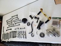 Overview of all hardware components laid out on a white surface, showing various black drawer pulls, shower/tub combo set parts, and a plastic bag of silver cabinet hinges.