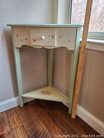 Front view of the small corner table showing the drawer with floral painted details and the lower shelf with a painted floral design.