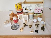 Photo displaying all the small decor items arranged on a white surface, including frames, figurines, salt and pepper shakers, cats, plate, piggy bank, and more.