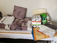 Display of assorted home soft goods including queen bedding with leaf pattern, fleece blankets, a beige pillow, two matching sheer curtains, and unopened Cal-King flannel sheet set.