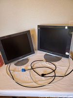 Front view of two Sony LED flat screen computer monitors, one smaller (17") and one larger (19") with power and VGA cables lying in front.