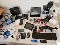 Wide view photo showing all items in lot including tablets, smartphones, cameras, chargers, earbuds, docking station and accessories laid out on flat surface.
