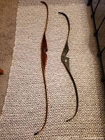 Two recurve bows, one brown and one green, laid flat on patterned carpet showing overall shape and length comparison