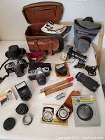 Wide view of both cameras, cases, bag, flashes, lens, filters, tongs, light meters and manuals arranged on table