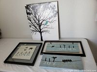 Four pieces of wall decor displayed on a table: two black framed prints and two stretched canvases, featuring blue birds and words LOVE, HOME, JOY, and a tree.