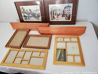 Photo showing front view of frames, prints, and two wooden wall ledges arranged on flat surface.