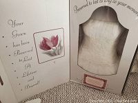View of preservation box with text indicating gown has been preserved to last a lifetime, partial view of dress inside box with floral image on inner flap.