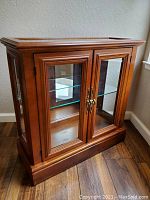Front view of wooden curio cabinet with glass panel doors and brass handles, showing the interior glass shelf and wood finish.