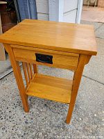 Front angled view of wooden Craftsman style side table showing drawer with black metal pull handle and bottom shelf.
