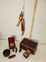 Photo of hand-carved wooden fish hanging on a metal line, two small carved cat figures, a wooden bowl, a wooden mortar and pestle, a small wooden box, and a boxed compass, along with a ruler for scale.