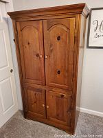 Front view of closed wooden pine armoire with four paneled doors and rounded top edges.