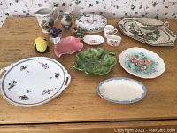 Photo of all 13 china and ceramic items on a wooden table, showing various decorative dishes, platters, and serving pieces.