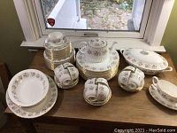 Full view of plates, cups, teapot, covered dish and platter arranged on table under window