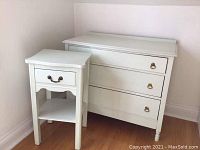 White dresser and matching nightstand positioned on hardwood floor against a corner wall.
