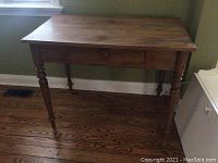 Front three-quarter view of the table showing turned legs and drawer face