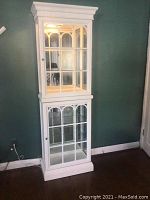Full view of tall white display cabinet showing both upper and lower compartments with glass doors and crown molding top.