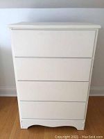 Front view of a white four-drawer dresser showing a simple, handle-less design with some minor wear.