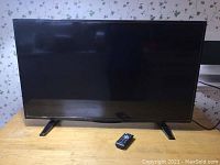 Front view of black 40 inch Insignia LCD TV on table with remote control in front.