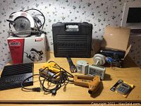 Full view of all tools on table showing Jobmate circular saw, heat tool, staplers, Kenwood amplifier, and boxed items.