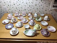 Overview of twenty assorted tea cups and saucers laid on wooden table, various floral designs and patterns visible