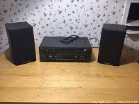 Full lot view with two Cerwin-Vega speakers positioned on either side of the Technics stereo receiver on a wooden surface with floral wallpaper background