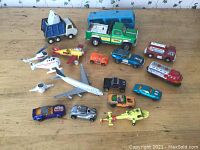 Multiple Matchbox Lesney toy vehicles and aircraft including trucks, cars, planes laid out on wooden surface showing condition and wear
