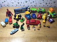 Full collection of various used toys, including vehicles and figurines, laid out on wooden surface.