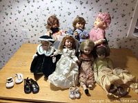 Seven vintage dolls arranged on wooden table with several separate doll shoes visible at front
