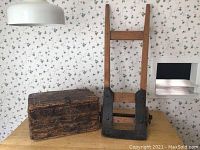Full view of vintage wooden toolbox next to vintage wooden hand truck dolly on table under hanging lamp
