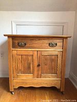 Front view of antique wooden cabinet showing drawer with metal handle, double doors with knob, and caster wheels.