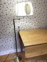 Brass floor lamp with round base and white fabric shade next to wooden table.