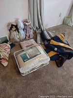 Lot of Earth Ragz blankets, quilt, towels, and three porcelain dolls displayed on carpeted floor near curtains and wall outlet.