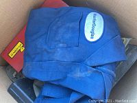 Photo of blue vintage Hunter Douglas coveralls with logo patch inside a cardboard box.