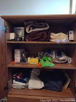 Photo of wardrobe shelves containing folded blankets, bed linens, and miscellaneous small boxed items.