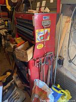 Side view of red and blue Craftsman rolling tool cabinet with stickers and hanging tools, showing the overall storage unit including multiple drawers and compartments.