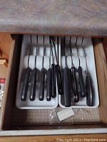 Eight piece cutter set and utensils with black handles in two white tray organizers inside drawer.