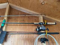 Three rods mounted horizontally on shed wall: two with reels attached, one blank rod.