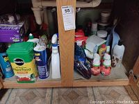 Photo showing assortment of cleaning and garden care products under sink including large containers, spray bottles, boxes of wipes or mop pads.