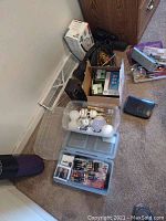 Photo showing assorted household items including lightbulbs in clear plastic bins, batteries in smaller cases, a cordless iron box, screwdrivers in a box, and a vacuum cleaner.