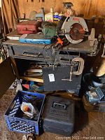 Overall view of workbench with tools including Craftsman circular saw, socket wrench case, auto chemicals in bottles, clamps and other hand tools.