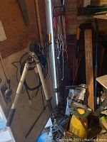 Metal garden loppers, extension cords, tools hanging on wooden wall hooks, various hand tools, and ice melt bag on floor near door in workshop/garage.